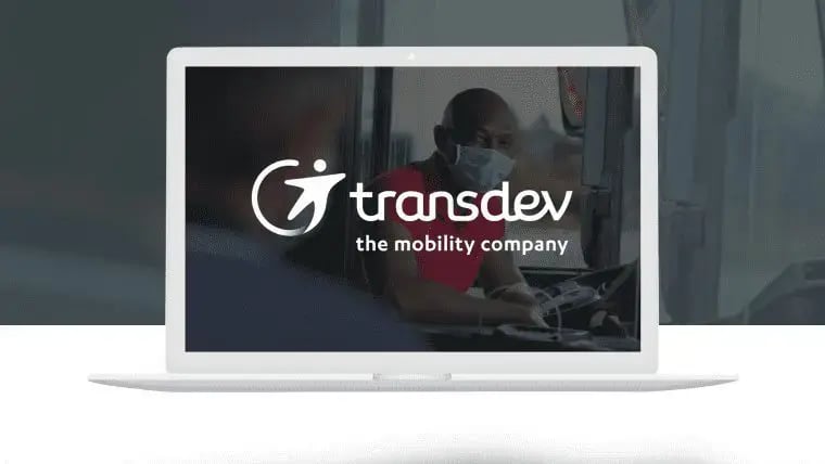 Vue du logo de Transdev sur un fond d'image où on voit un conducteur d'autobus.